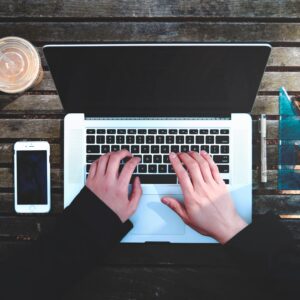 man typing on Macbook next to iPhone and coffee cup