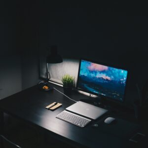 desk with lamp, pen, notepad, Macbook, desktop monitor, and keyboard