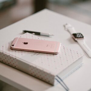 iPhone resting on book next to Apple watch and pen