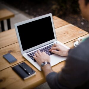 hands typing on Macbook on table with phone and notepad