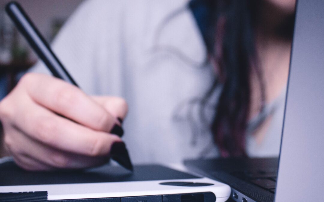 woman writing on tablet next to laptop